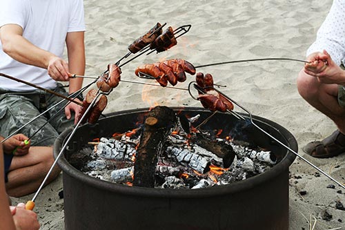 People barbecuing meat over a beach fire